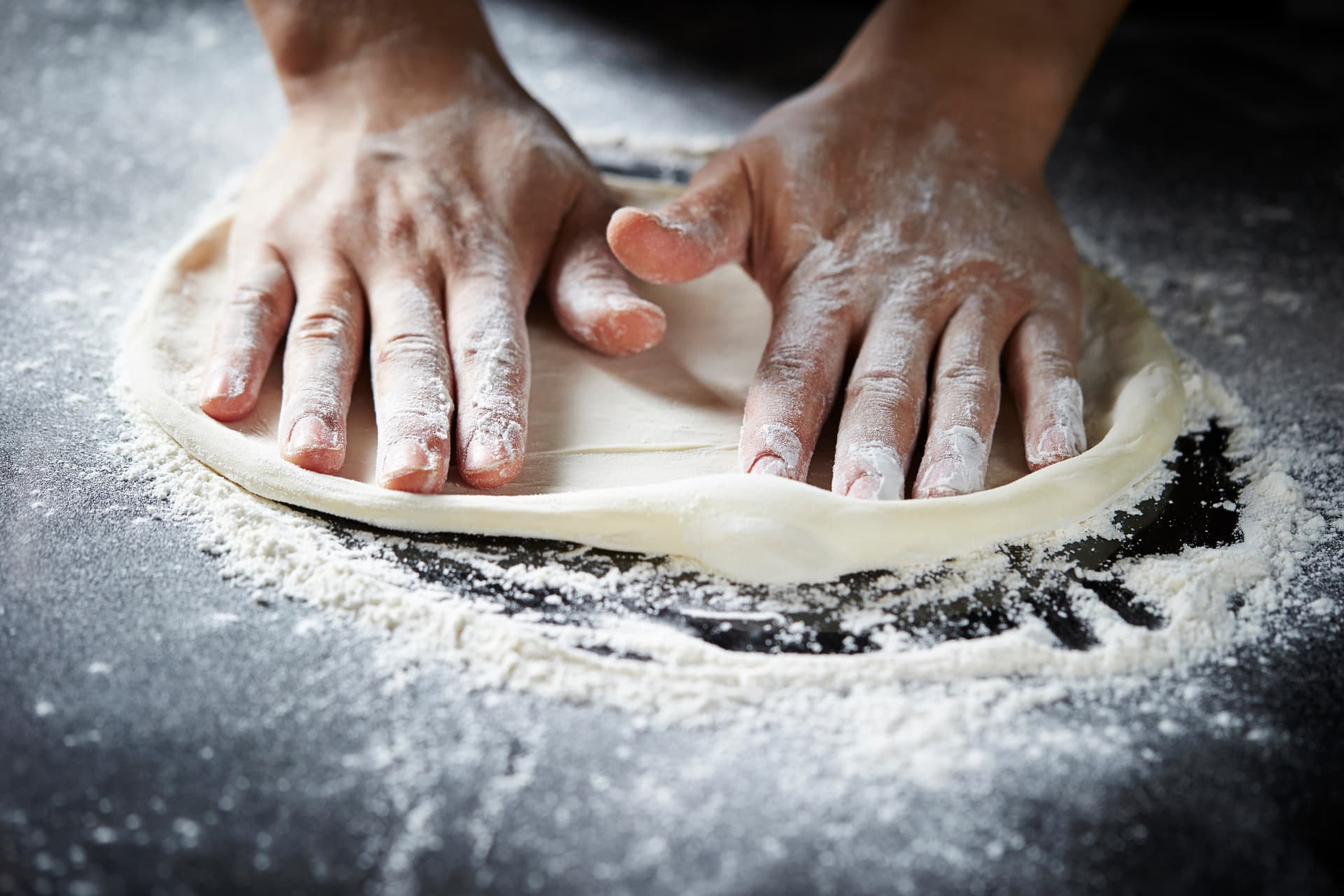 Bagare som formar pizzadeg för hand på mjölat bord